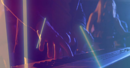 Playing musician's hands pressing synth keyboard on club stage, in dark long sleeves, with LED bars....