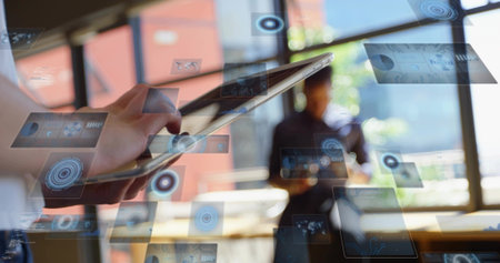 Swiping foreground hand wearing light sleeve on tablet in modern office, showing HUD panels....