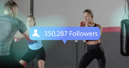 Training coach holding mitts, two women in gear boxing at gym, heavy bag, 350,287-Followers overlay....