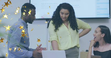 Leaning center woman in yellow blouse reviewing laptop in meeting with wall display, gold stars....