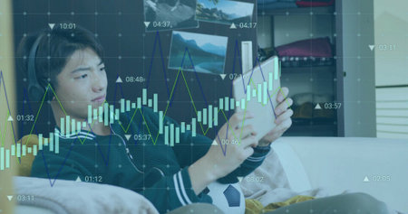 Holding tablet teen wearing pullover and headset reclining on couch with soccer ball, chart overlay....