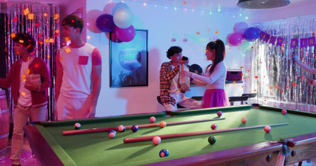 Handing woman wearing pink skirt passing trophy to seated man on pool table at birthday party....