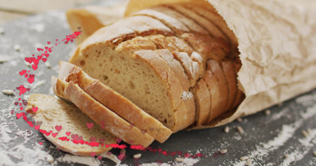 Showing rustic sliced loaf resting in crumpled paper bag on slate, flour-dusted with pink hearts....