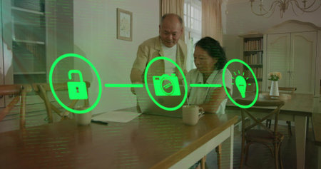 Reviewing senior couple wearing cardigans using laptop at dining area, with smart-home icons, mugs....