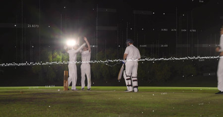 Celebrating fielders raising arms, batsman in white kit with bat on night pitch near stumps, data....