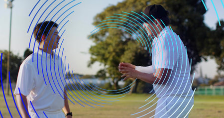 Talking men wearing white polos and shorts, gesturing on park field near shore with blue rings....