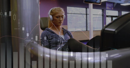 Exercising woman in zip jacket, headset pushing legs on recumbent machine at gym with chart overlay....