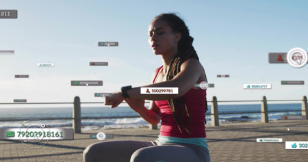 Checking woman wearing maroon tank and gray leggings tapping smartwatch on tiled seaside data tags....