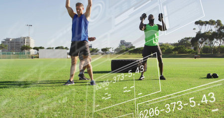 Performing overhead lifts two men in blue and green tops on grass with tire, dumbbells, overlays....