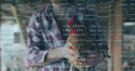 Cradling brown red-combed hen, plaid-shirt man in dark apron standing in barn, financial overlay....