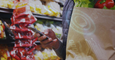 Holding man checking phone while carrying paper bag with produce in store aisle, red snacks, vest....