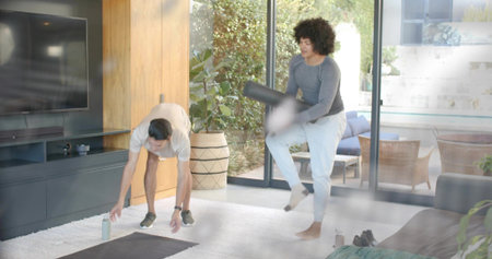 Bending man reaching water bottle and friend holding foam roller, working out in sportswear at home....