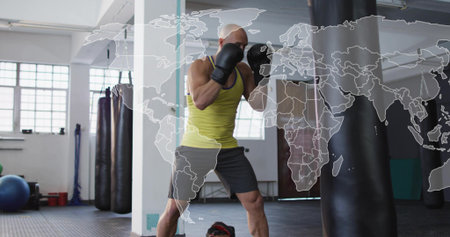 Punching bald man wearing yellow tank, black gloves training in gym with heavy bag, map overlay....