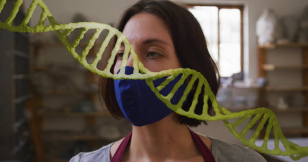Standing woman wearing navy mask and maroon apron in studio with pottery shelves, green DNA overlay....