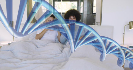 Smiling two men wearing light shirts sitting in bed holding phones, blue DNA overlay and lamps....