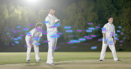 Posing three men in white on night pitch wearing gloves, floodlit, magenta or cyan light. Cricket,...