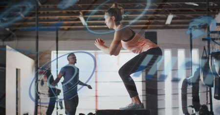 Balancing woman wearing pink tank performing plyometric box jump in warehouse gym, with jump rope....