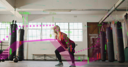Squatting woman in boxing studio in pink tank, black tights, with kettlebell, bags, data overlays....