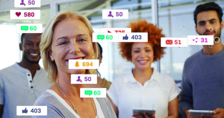 Smiling team lead standing in open office with tablets and social alerts, wearing business casual....