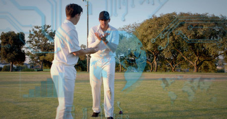 Holding red cricket ball, two players wearing white kit on sports field, showing digital overlay. Athletes, outdoor, uniforms, training, teamwork, grass, capの写真素材
