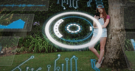 Leaning against tree trunk woman in pink top holding smartphone on lawn, HUD circuits, copy space....