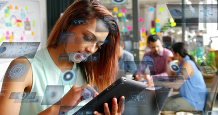 Using tablet, woman wearing sleeveless top interacting with holographic UI in open-plan office....