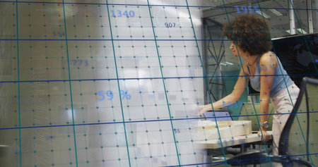Leaning worker checking laptop at open office with grid overlay, in sleeveless blue top, copy space....
