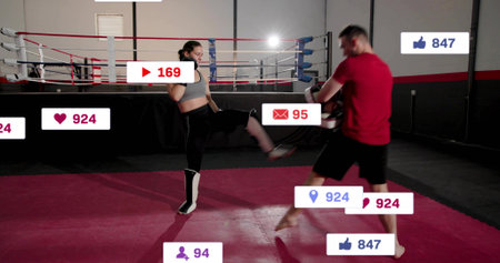 Executing athlete in gray top, shin guards kicking trainer in ring with focus mitts, social-icons....