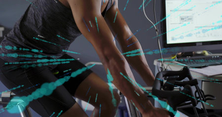 Cycling male wearing dark tanktop and cycling shorts on stationary bike in home gym, monitor charts....