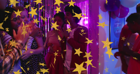 Clapping friends hugging, holding cups in party room with metallic fringe, balloons, pink dress....