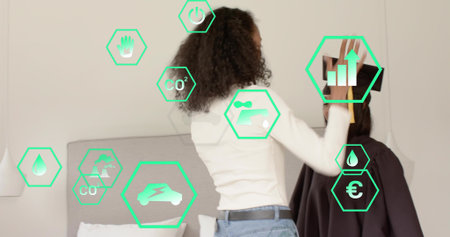 Placing woman in white-top fitting black headset on friend in dark cape in bedroom, green AR-icons....