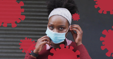 Adjusting woman in burgundy sweater pulling surgical mask ear loops on street, red virus overlays....