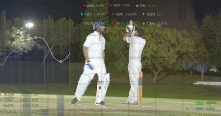Adjusting helmet, two players in white kits at crease under floodlights, showing stumps and data....