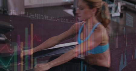 Rowing mid-adult woman powering stroke at gym on rower with data charts overlay, wearing blue bra....