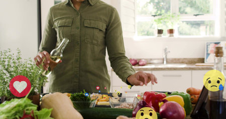 Holding oil bottle, adult woman wearing olive shirt prepping vegetables in kitchen with tablet....