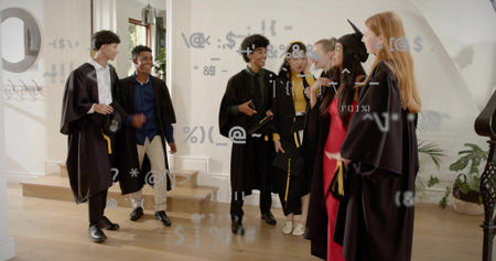 Chatting six graduates wearing black gowns holding diplomas in residential foyer, with mortarboards....