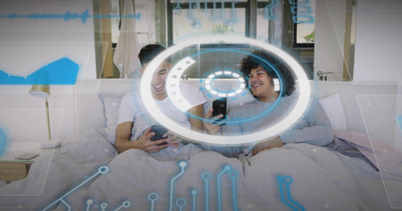 Laughing friends sitting on bed wearing white tee gray top holding gamepad and phones with HUD....