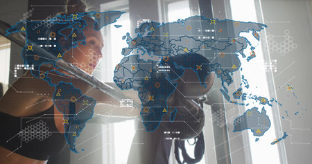 Training woman in black-sports-bra and wraps striking heavy bag in gym by windows chain data-map....