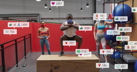 Squatting man wearing face mask and sportswear on wooden plyo box at gym, with social overlays....