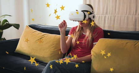 Wearing white VR headset, woman gesturing at home on sofa in red t-shirt, jeans, gold stars....