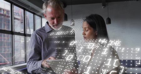Reviewing colleagues wearing business wear in loft, studying tablet with binary overlay and windows....
