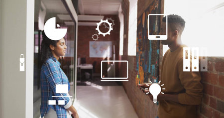 Talking coworkers leaning by glass wall in office, in casual clothes, holding phone with UI icons....