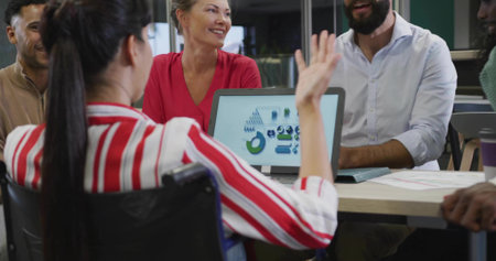 Pointing woman in striped blouse presenting laptop charts at office meeting, team listening....