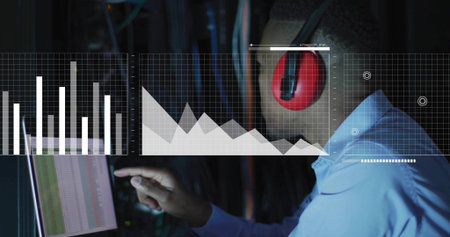 Pointing tech in light blue shirt, red headset, touching data-center screen with charts, copy space....