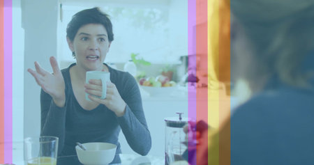 Talking woman in dark gray top gesturing in kitchen, with mug, bowl, orange juice, French press....