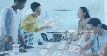 Four women gesturing and writing in meeting room with papers, laptop, yellow sweater, data overlay....