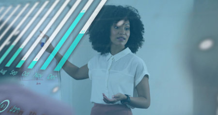 Presenting woman in blouse, skirt pointing at bar chart on glass board, meeting room, blurred left....