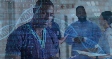 Smiling male in scrubs writing notes in clinic corridor, with clipboard, lanyard and DNA overlay....