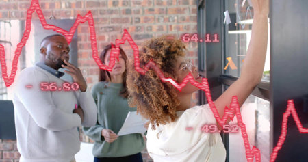 Writing curly woman holding marker on glass board at office, in light top showing red graph....