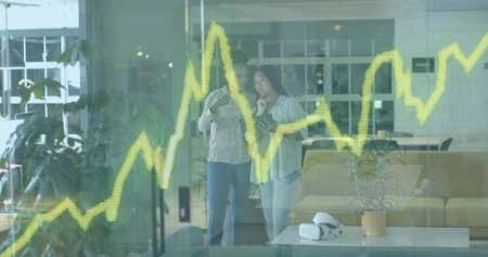 Reviewing tablet, two women in biz-casual in office lounge, by glass showing yellow-green chart....